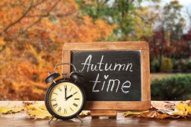 Alarm saati, yazı tahtası AUTUMN Time ve açık masa üzerinde yapraklar