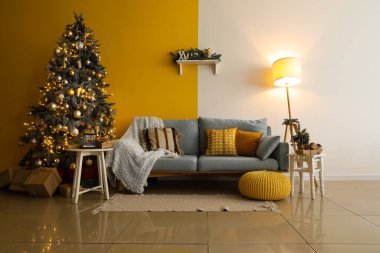 Gri kanepe, Noel ağacı ve sarı duvarlı modern oturma odasında parlayan lamba.