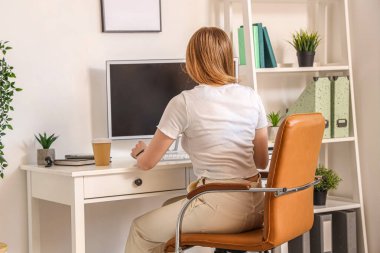 Ofisteki masada bilgisayarla çalışan genç bir kadın.