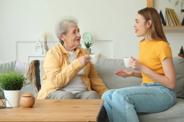 Büyükannesiyle birlikte evdeki kanepede çay içen genç kadın.