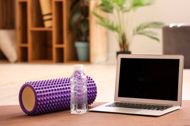 Bir şişe su ve köpük kaplı dizüstü bilgisayar. Odadaki spor paspası.