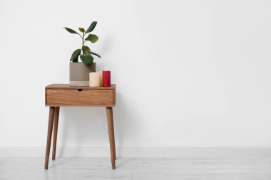 Odadaki ışık duvarının yanındaki masada mumları olan yeşil bitki.