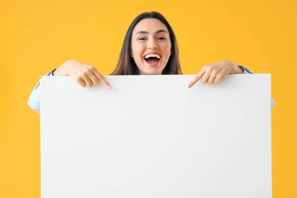 黄色の背景に大きな空白のポスターを指している幸せな若い女性 — ストック写真