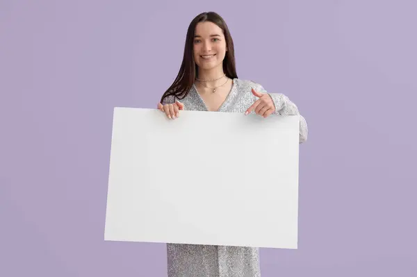 穿着闪亮衣服的年轻女子指着淡紫色背景上空白的大海报 — 图库照片