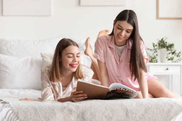 Female friends reading magazine in bedroom