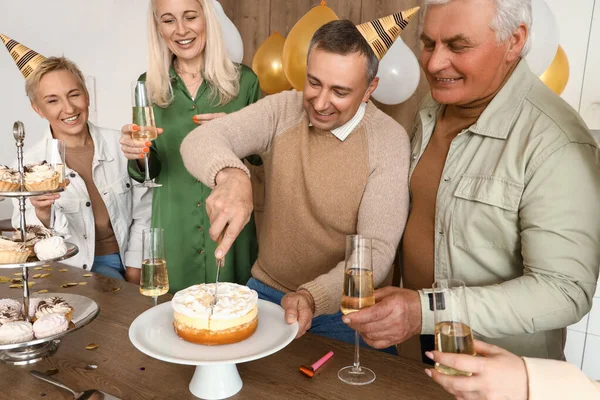 Mature man cutting Birthday cake for his friends at party in kitchen