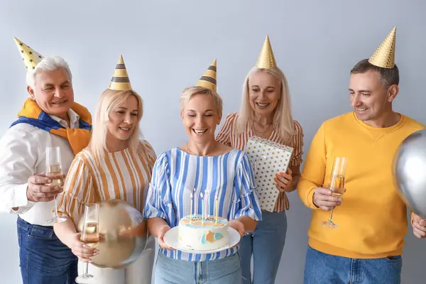 Mature people with cake and champagne celebrating Birthday on light background