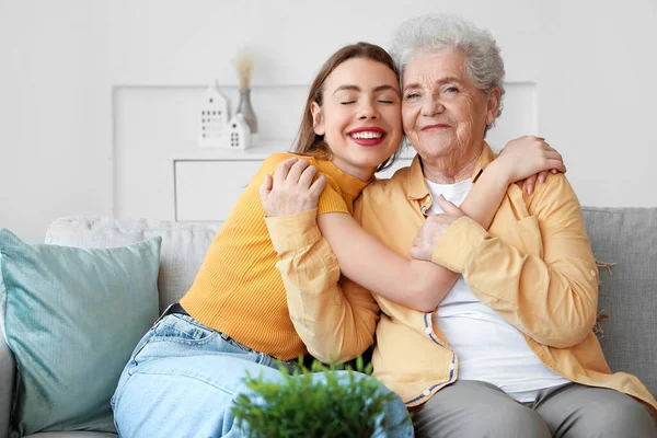 Young woman with her grandmother hugging on sofa at home