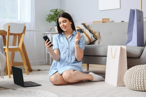 Young woman with credit card and mobile phone shopping online at home