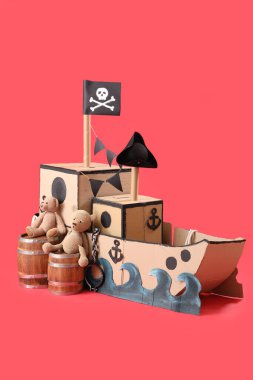 Kırmızı arka planda varilleri ve oyuncak ayıları olan korsan karton gemi.