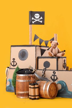 Sarı arka planda oyuncak ayı ve varilleri olan korsan karton gemi.