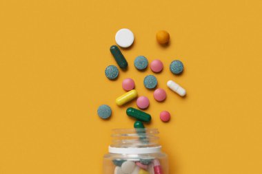 Turuncu arka planda farklı dağıtılmış haplarla dolu kavanoz.