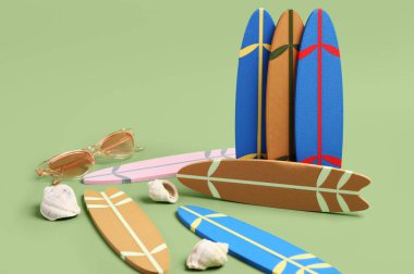 Farklı küçük sörf tahtaları, güneş gözlükleri ve yeşil arka planda deniz kabukları.