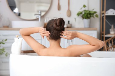 Genç bir kadın evde banyo yapıyor, arkadan bakıyor.