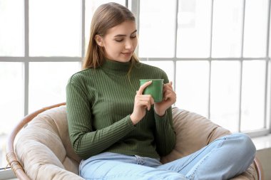 Bir fincan sıcak çayla evdeki koltukta oturan genç bayan.