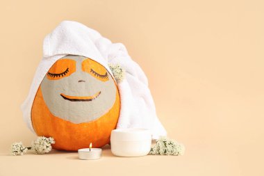 Kil maskeli balkabağı, havlu, krema ve yanan mum bej arka planda