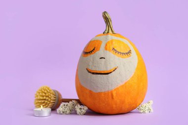 Kil maskeli balkabağı, çiçekler, mum ve arkaplanda masaj fırçası