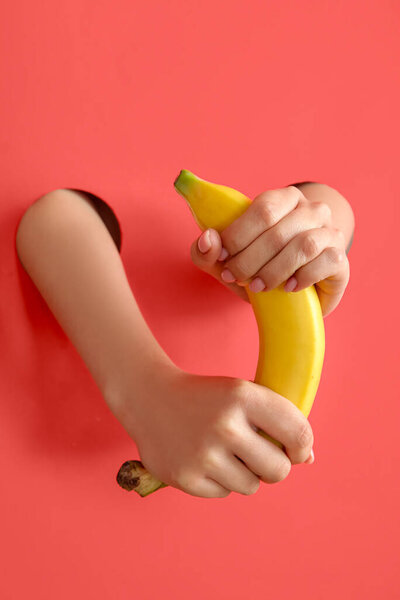 Female hands with fresh banana on red background. Sex education concept