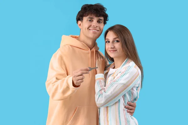 Young couple with key from house on blue background