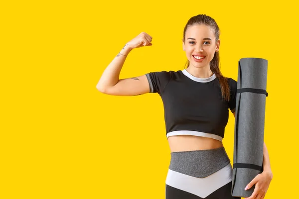 Sportliche Junge Frau Mit Fitnessmatte Zeigt Muskeln Auf Gelbem Hintergrund — Stockfoto