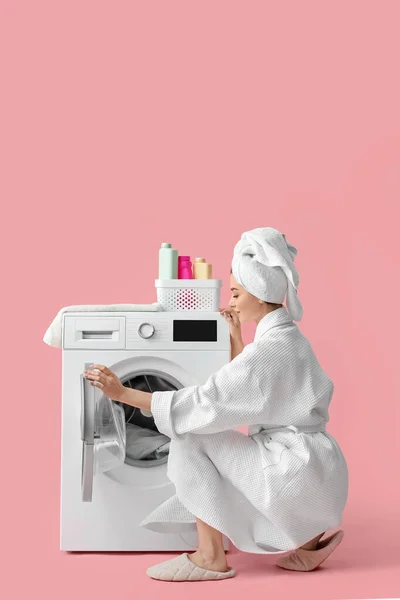ピンクの背景に洗濯機が付いているバスローブの若い女性 — ストック写真