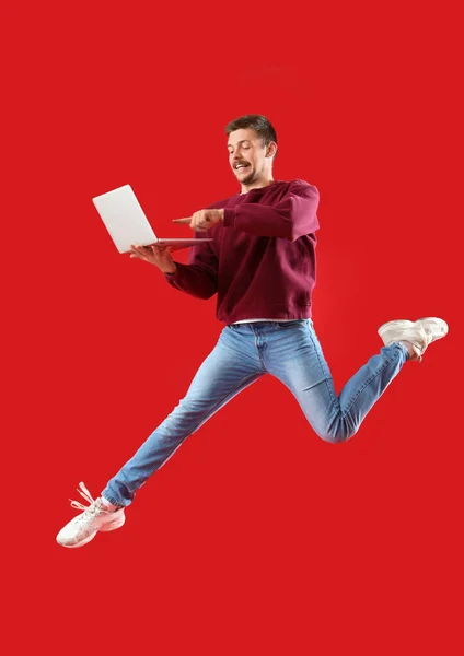 Skoky Mladý Muž Notebookem Červeném Pozadí — Stock fotografie