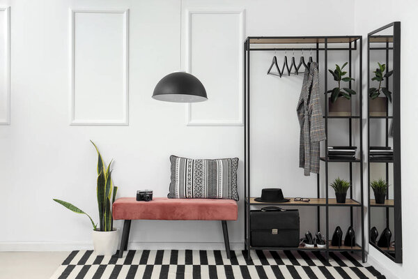 Interior of stylish hall with soft bench and clothes rack
