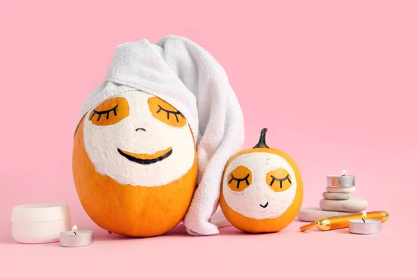 Pumpkins with masks, spa stones, cream and burning candles on pink background