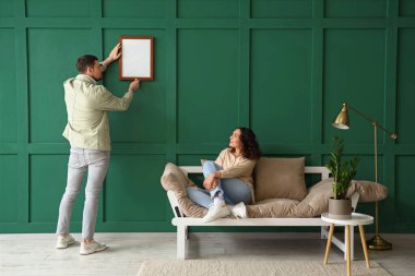 Evdeki yeşil duvara boş bir çerçeve asan genç çift