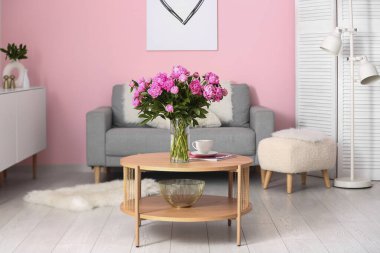 Kahve masasında pembe şakayık vazosu ve oturma odasında kanepe.