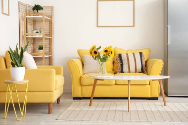 Güzel ayçiçekli vazo, sarı kanepe ve şık oturma odasının içinde koltuk.