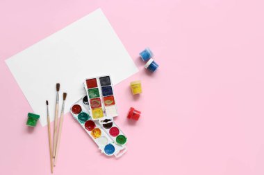 Suluboya resimler, fırçalar ve pembe arka planda boş kağıtlar.