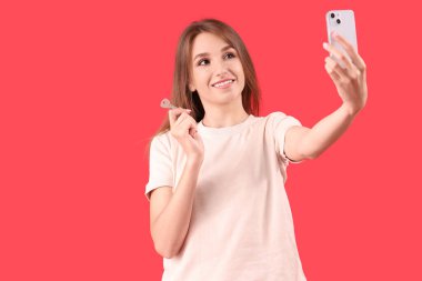Evdeki anahtarı olan genç bir kadın kırmızı arka planda selfie çekiyor.
