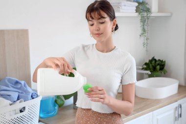 Çamaşır deterjanıyla evde çamaşır yıkayan genç bir kadın.