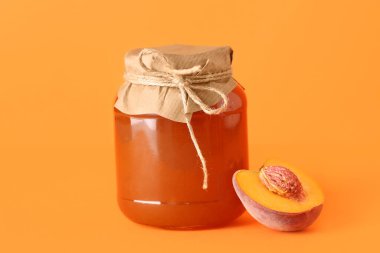 Tatlı şeftali reçelli kavanoz ve turuncu arka planda taze meyve.