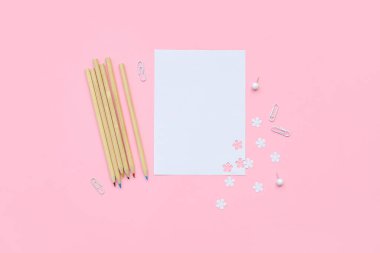 Pembe zemin üzerinde boş kağıt, renkli kalemler ve ataçlarla kompozisyon