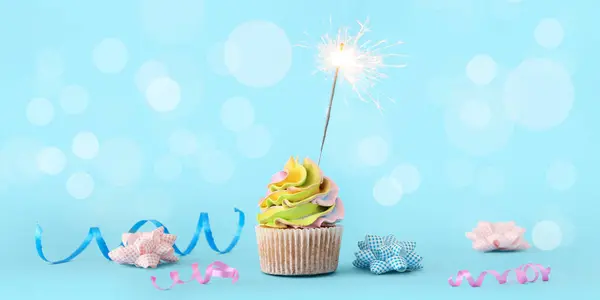 Tasty birthday cupcake with sparkler and decor on light blue background