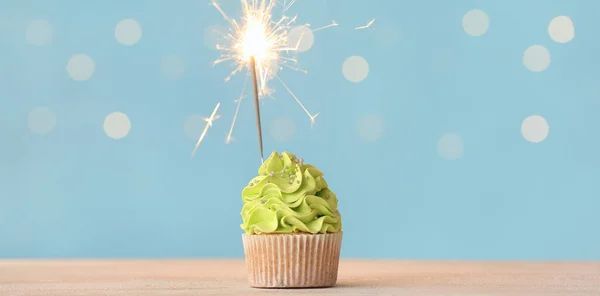 Tasty cupcake with sparkler on light blue background