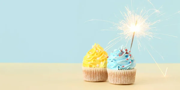 Tasty cupcakes with sparkler on light blue background with space for text