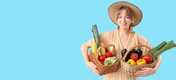 テキスト用のスペースを持つライトブルーの背景に異なる野菜でいっぱいのウィッカーバスケットを持つ若い女性農家 — ストック写真