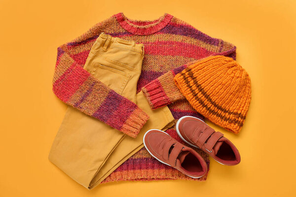 Warm children's clothes and shoes on color background