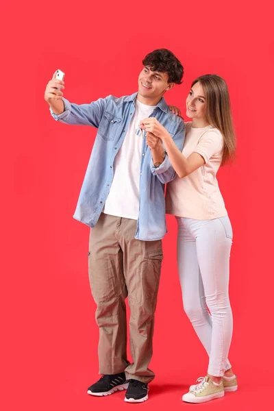 Young couple with key from house taking selfie on red background