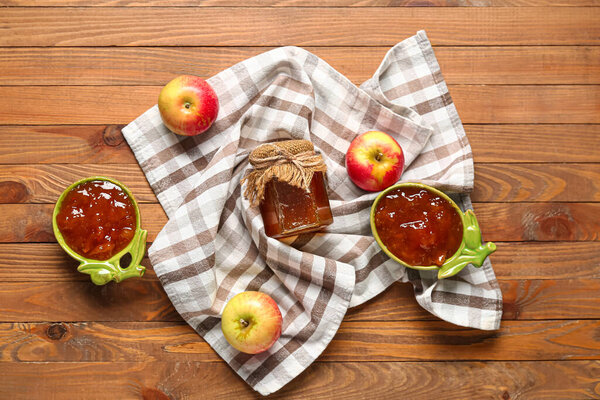 Bowls and jar of sweet apple jam on wooden background