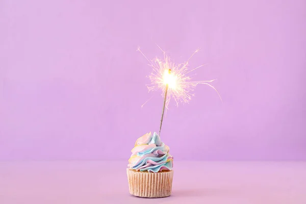 Tasty birthday cupcake with sparkler on purple background