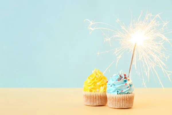 Tasty birthday cupcakes with sparkler on blue background