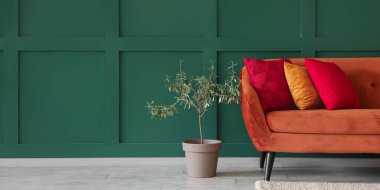 Yeşil duvarın yanında şık minderleri ve çiçekleri olan rahat bir kanepe. Tasarım için pankart