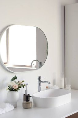 Banyodaki beyaz lavabo, banyo aksesuarları ve çiçekler.