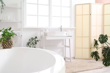 Lavabosu, küveti, raf ünitesi ve çiçekleri olan hafif banyonun içi.