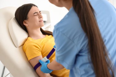 Kadın hemşire klinikte genç bir donörü kan nakline hazırlıyor.