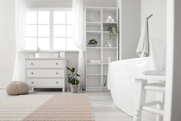 Stock image Interior of light bathroom with sink, bathtub, shelving unit and houseplants